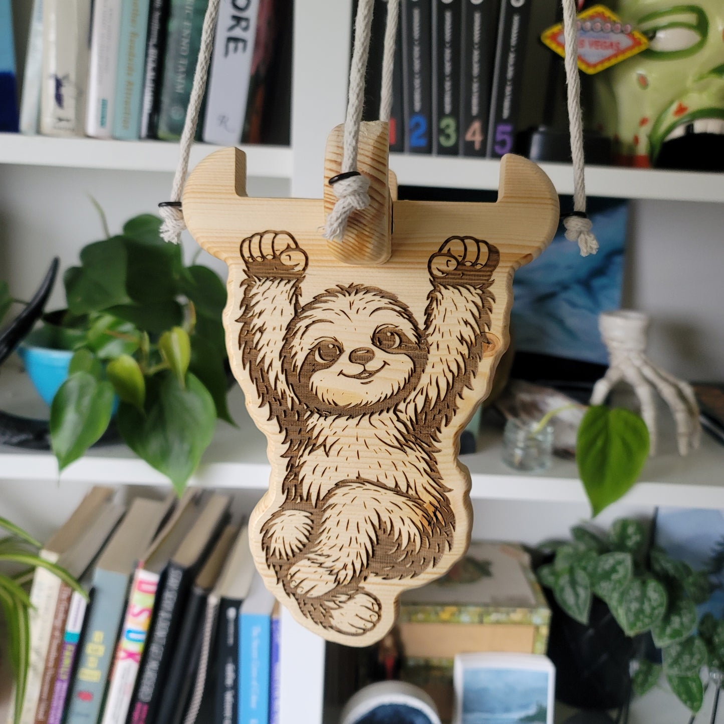 Wooden sloth ornament on a bookshelf with books and plants in the background