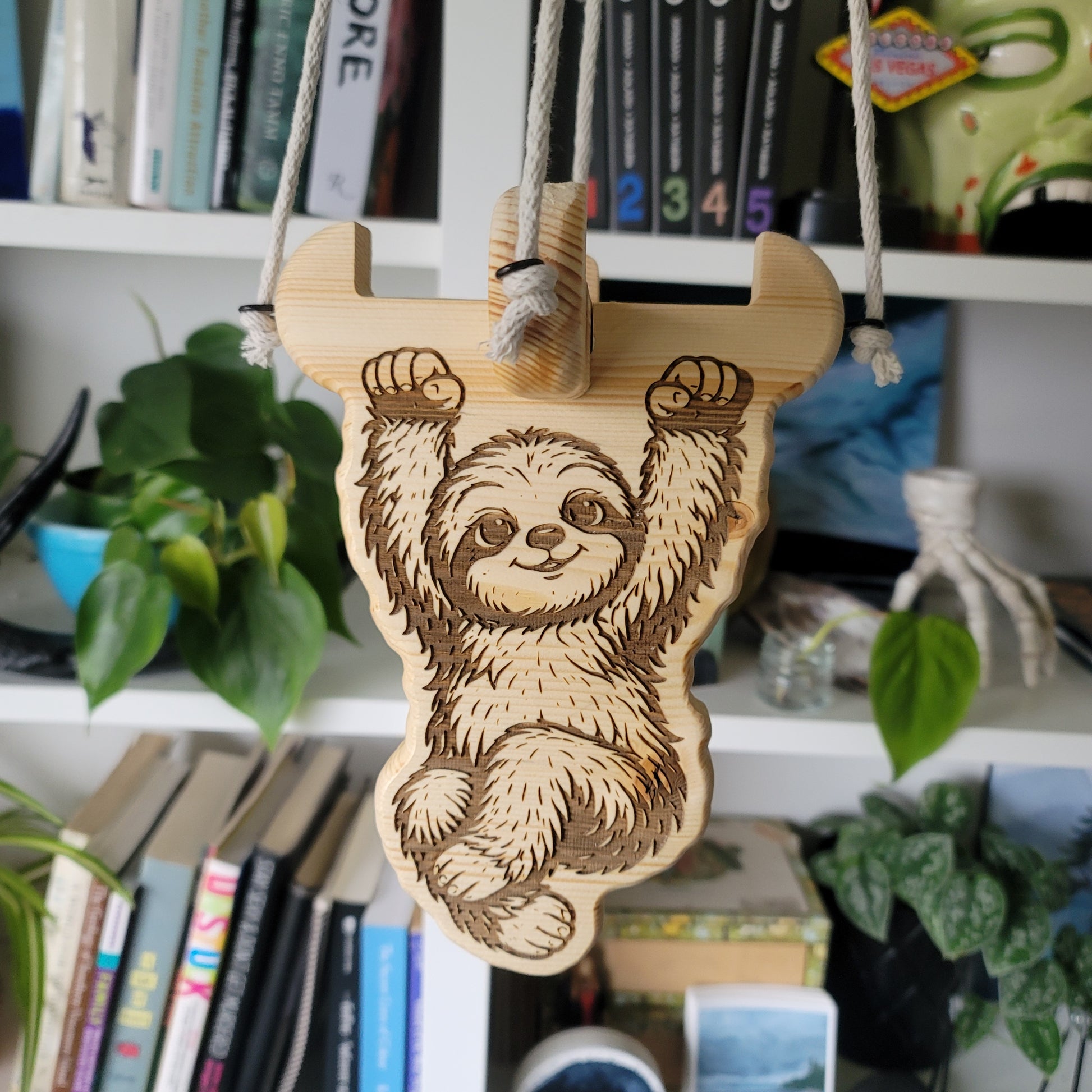 Wooden sloth ornament on a bookshelf with books and plants in the background