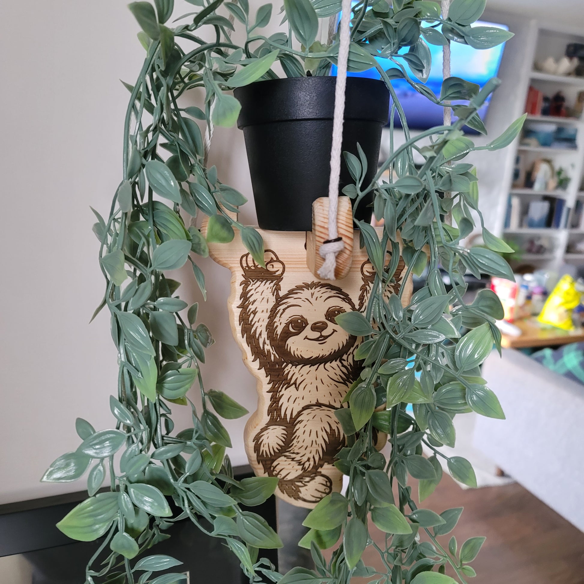 sloth plant hanger surrounded by green leaves on a blurred indoor background