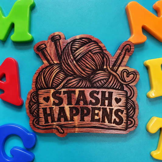 A wooden plaque or coaster featuring a hand-painted design of yarn balls on knitting needles and the text 'STASH HAPPENS' in dark brown lettering, set against a bright turquoise background with colorful plastic letters around it.
