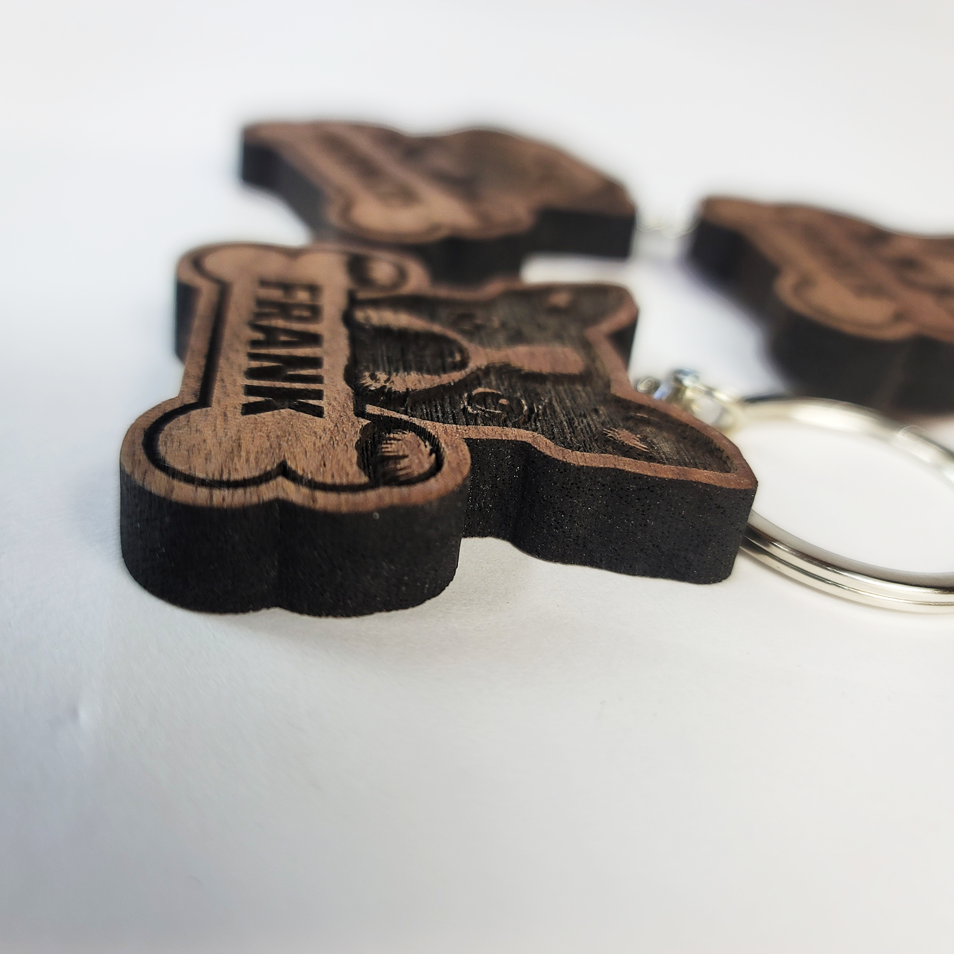 Wooden dog tag keychain with 'FRANK' engraved on a white background