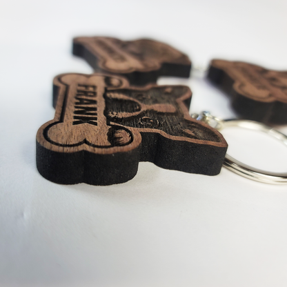 Wooden dog tag keychain with 'FRANK' engraved on a white background